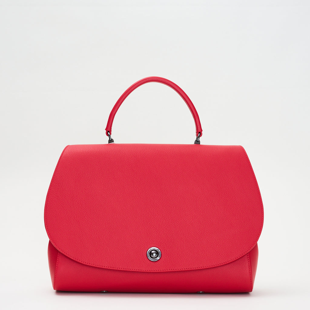 The product photo of a colorful red top handle leather handbag. The handbag has a minimalistic design and an oversized round flap cover. This is the Tomoli Briffani Jut interchangeable satchel in Red.