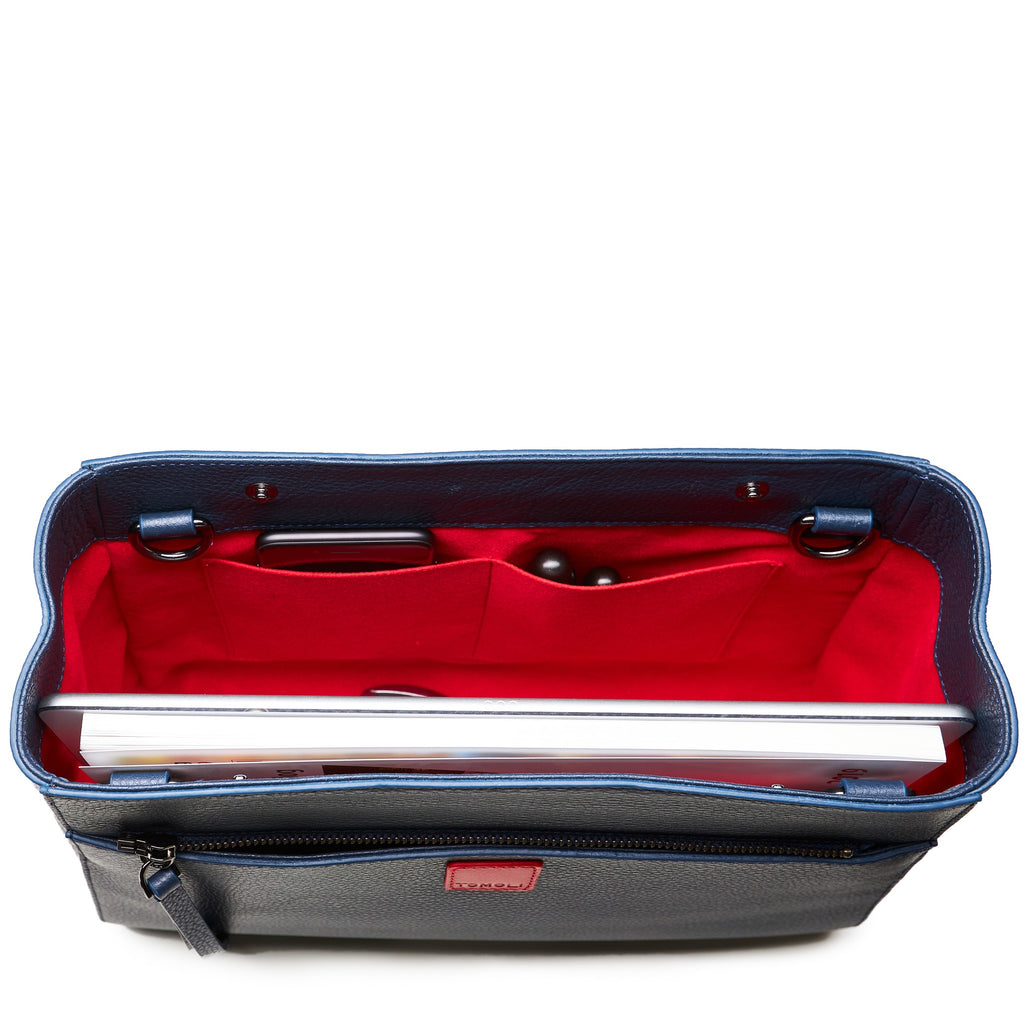 The product photo of a fashion handbag showing the interior of a dark blue leather bag. The bag has a bright red lining made of alcantara microsuede material. This is the interior view of the Tomoli Briffani Jut handbag in Flirty Denim. This bag fits a laptop and a large iPad Pro tablet.