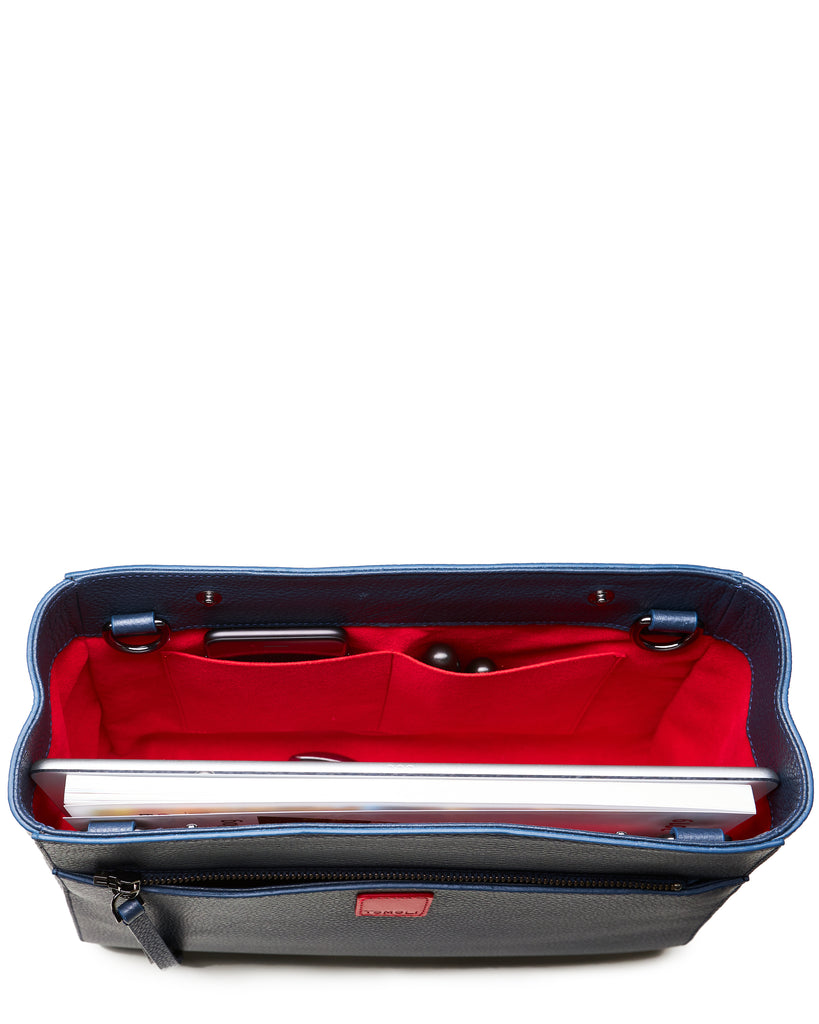 The product photo of a fashion handbag showing the interior of a dark blue leather bag. The bag has a bright red lining made of alcantara microsuede material. This is the interior view of the Tomoli Briffani Jut handbag in Flirty Denim. This bag fits a laptop and a large iPad Pro tablet.