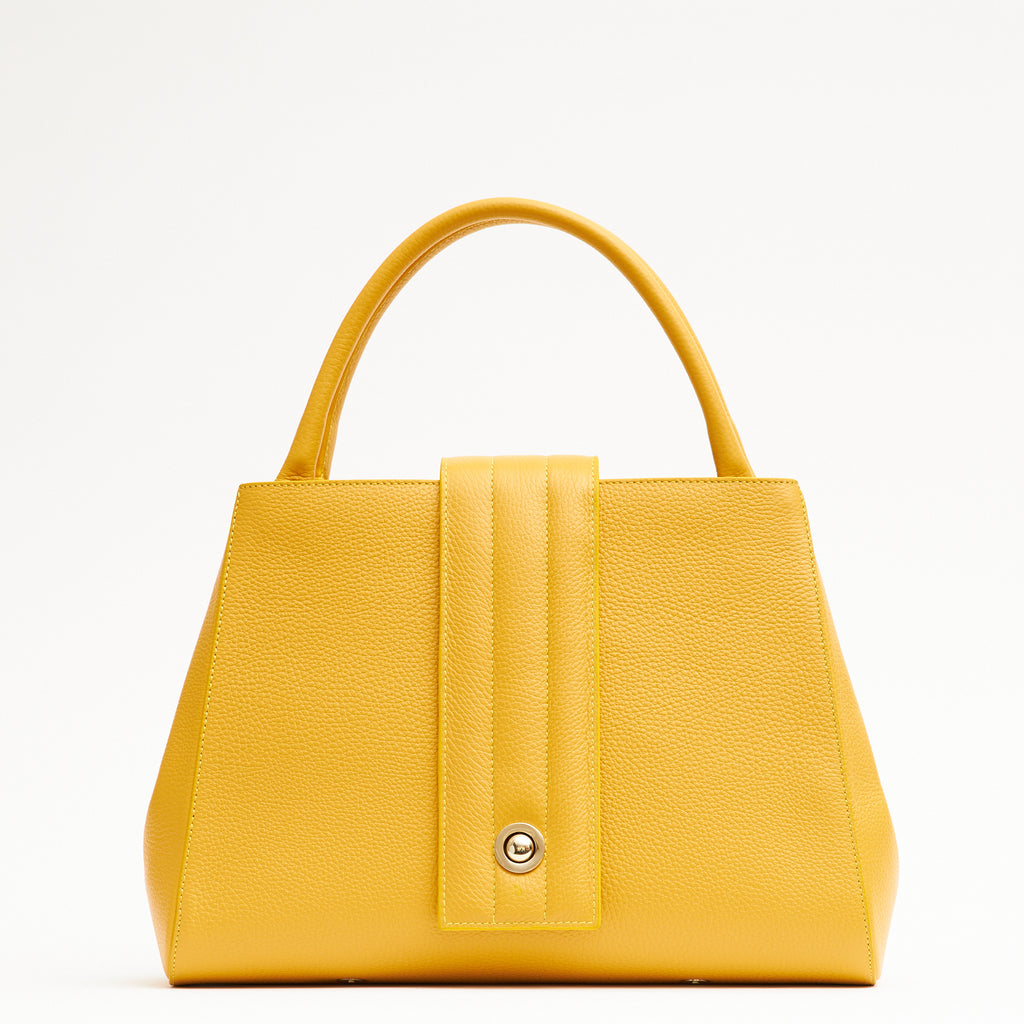 A product photo showing the front view of a colorful yellow leather handbag. The handbag has a classic trapeze shape with yellow top handles and a straight quilted flap in the middle. This is the Tomoli Briffani Lean interchangeable tote handbag in Maize. This bag can be used as an everyday bag, a work tote, or even an oversized clutch.