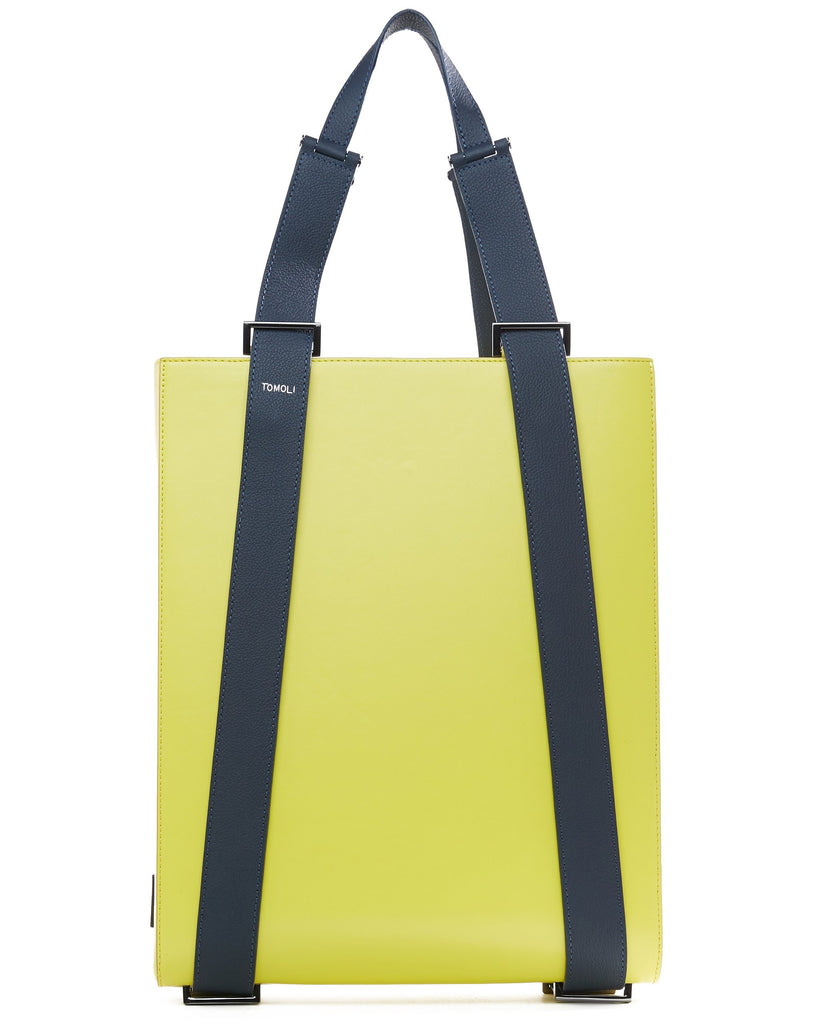 A product photo of a lime green leather tote bag. The tote bag has a structured rectangular briefcase shape and color-blocked dark blue leather straps. This is the front view of the Tomoli Kora large convertible leather tote in shady chartreuse. The bag can fit a laptop and can be styled for work or to elevate casual outfits.