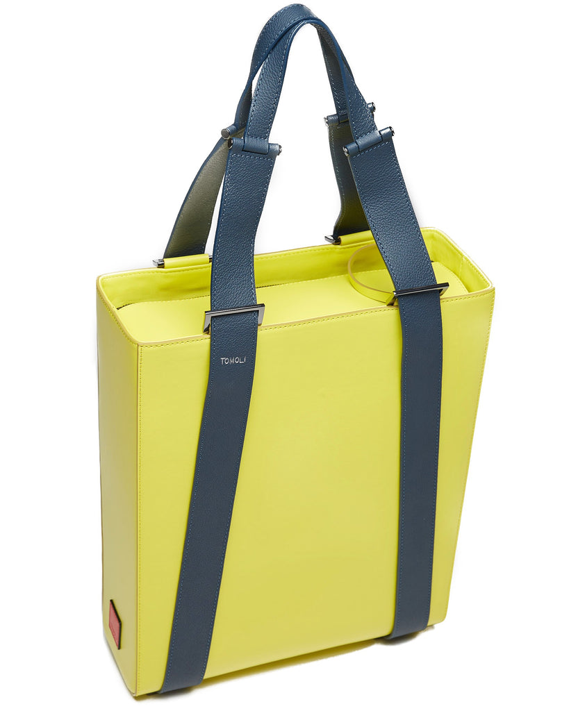 A product photo of a lime green leather tote bag. The tote bag has a structured rectangular briefcase shape and color-blocked dark blue leather straps. This is the top view of the Tomoli Kora large convertible leather tote in shady chartreuse. The bag can fit a laptop and can be styled for work or to elevate casual outfits.