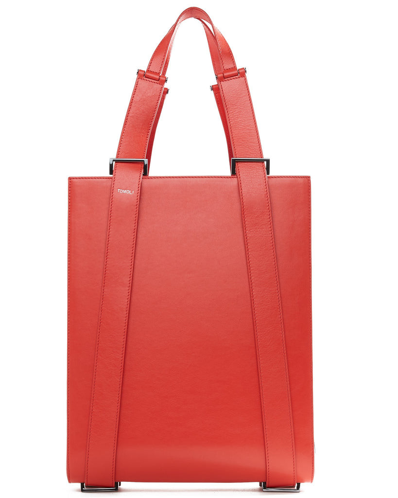 A product photo of a red leather tote handbag. The tote has a structured rectangular shape and flat handles. This is the Tomoli Kora tote in red aria leather. This bag can be used as a work bag or an everyday bag.