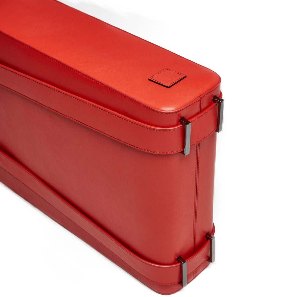 A product photo showing the bottom of a red leather tote handbag. The tote has a structured rectangular shape and flat handles. This is the Tomoli Kora tote in red aria leather. This bag can be used as a work bag or an everyday bag.