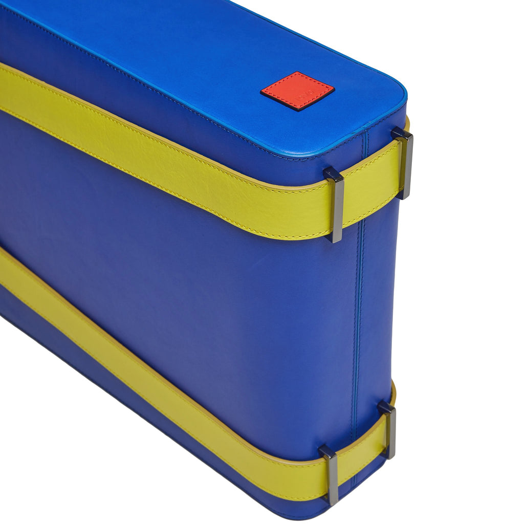 A product photo of a bright blue leather tote bag. The tote bag has a structured rectangular briefcase shape and color-blocked neon green leather straps. This is the bottom view of the Tomoli Kora large convertible leather tote in lime blue. The bag can fit a laptop and can be styled for work or to elevate casual outfits.