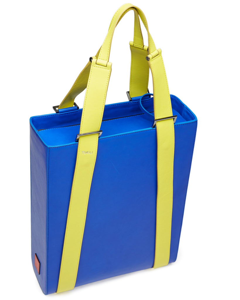 A product photo of a bright blue leather tote bag. The tote bag has a structured rectangular briefcase shape and color-blocked neon green leather straps. This is the top view of the Tomoli Kora large convertible leather tote in lime blue. The bag can fit a laptop and can be styled for work or to elevate casual outfits.