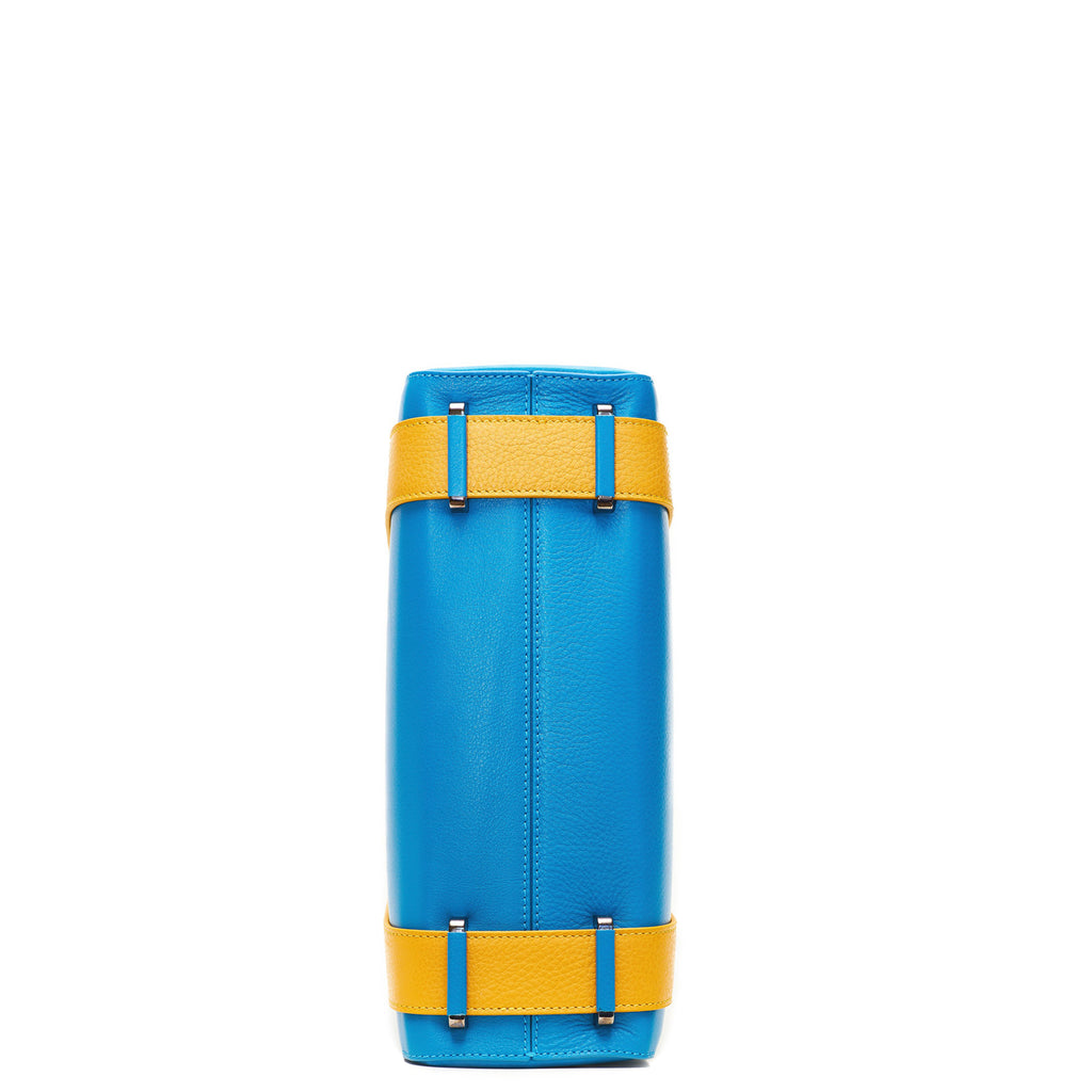 A product photo showing the bottom view of a turquoise blue leather tote. The bottom shows a center seam and color-blocked yellow straps. This is the Tomoli Kora large convertible leather tote in Golden Sky.