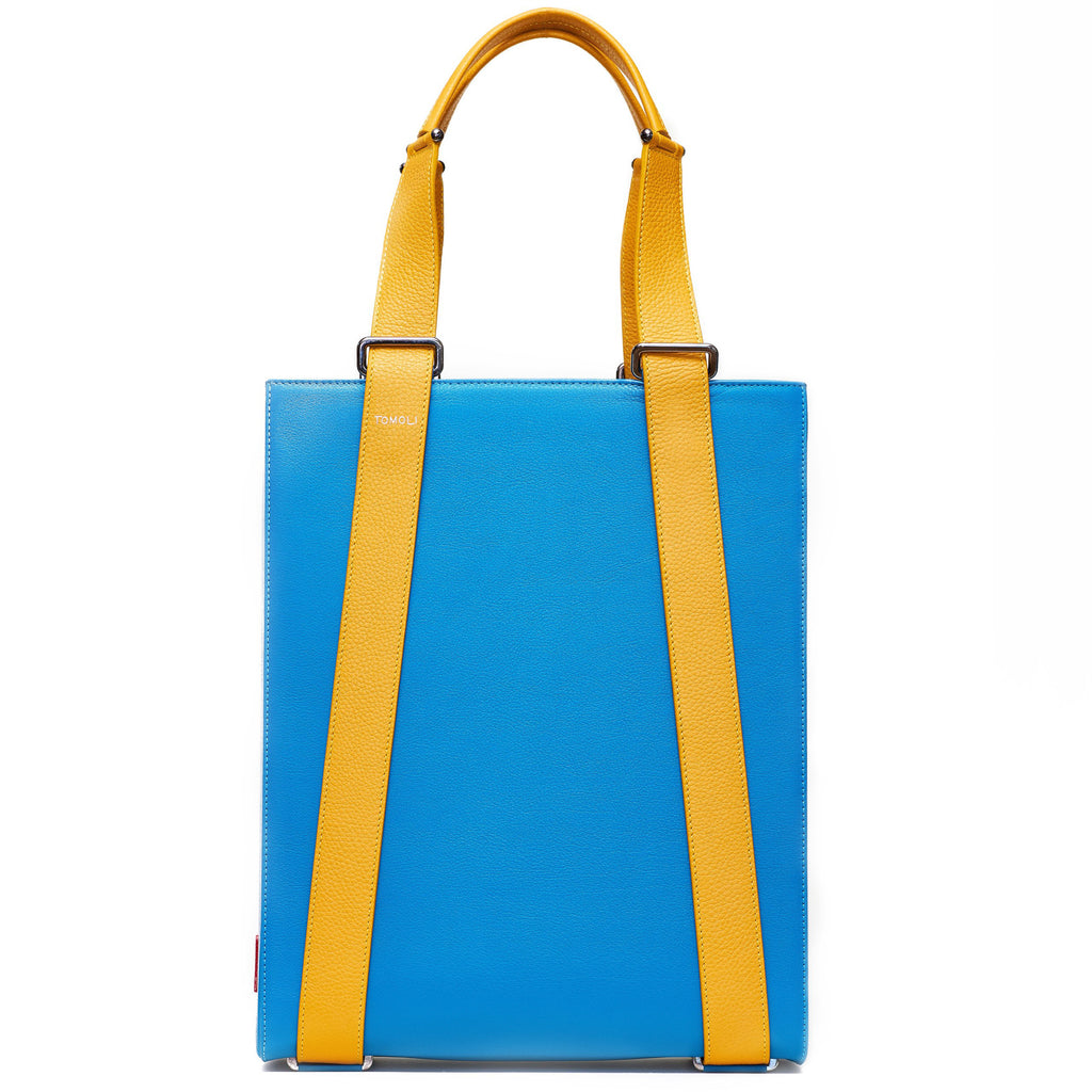 The product photo of a turquoise blue leather tote bag. The tote bag has a structured rectangular briefcase shape and is color-blocked with yellow leather straps. This is the front view of the Tomoli Kora large convertible leather tote in Golden Sky. The bag can fit a laptop and can be styled for work or to elevate casual outfits.