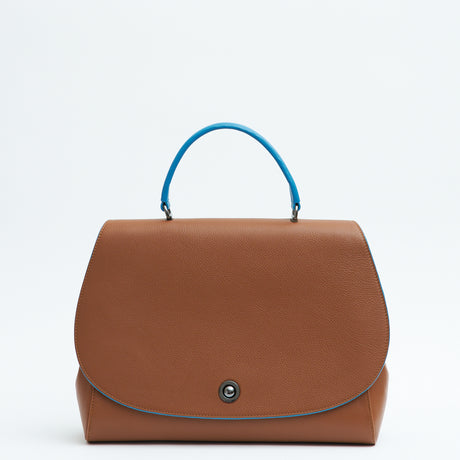 The product photo of a colorful brown top handle leather handbag. The handbag has a minimalistic design and features an oversized rounded flap cover that is color-blocked with a blue top handle. The edges of the flap cover are painted in a contrasting blue color. This is the Tomoli Briffani Jut interchangeable satchel in Sky Pecan.