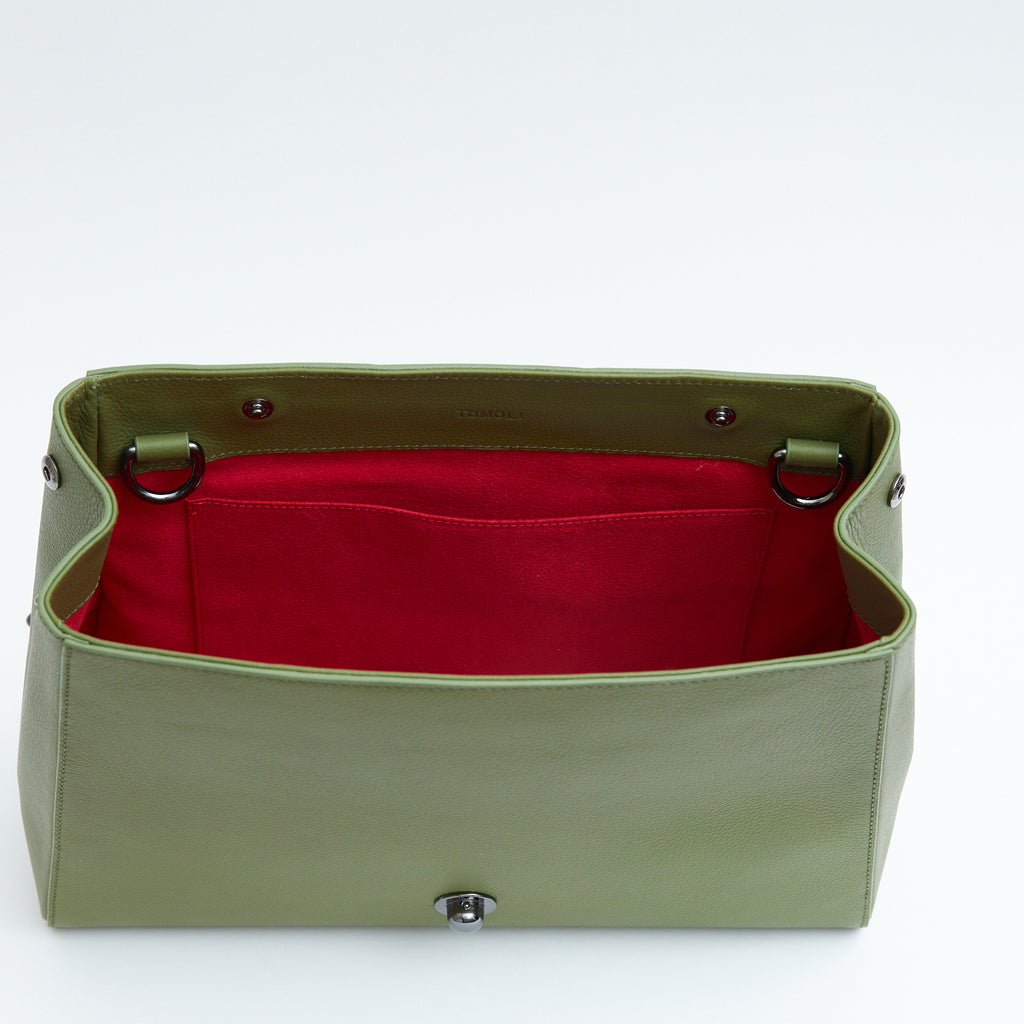 The product photo of an olive green leather handbag. The handbag has a classic trapeze shape with a back pocket, a zipper to interchange flaps, and top handles. This is the back view of the Tomoli Briffani Lean interchangeable tote handbag in Olive Green. This bag can be used as an everyday bag, a work tote, or even an oversized clutch.