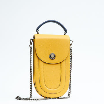 A fashion product photo showing the front view of a colorful yellow leather handbag. The bag has an elongated rounded shape that resembles a saddle bag. The handbag has a flap closure with dark blue trims and a dark blue handle. There is a chain strap and a metal lock in gunmetal hardware. This is the Tomoli Fitini II structured saddle handbag in Shady Maize. This handbag can be used as an everyday crossbody bag, a work bag, or a special occasion bag.
