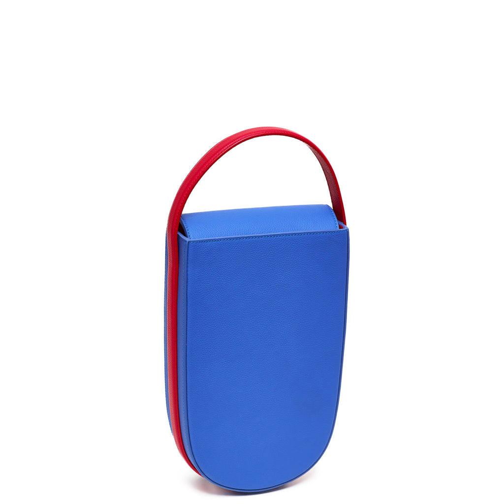 A colorful red and blue mini leather tote handbag. The handbag has an elongated rounded shape and a red adjustable top handle. The hardware is gunmetal. This is the front view of the Tomoli Fitini bag in Hot Iris.