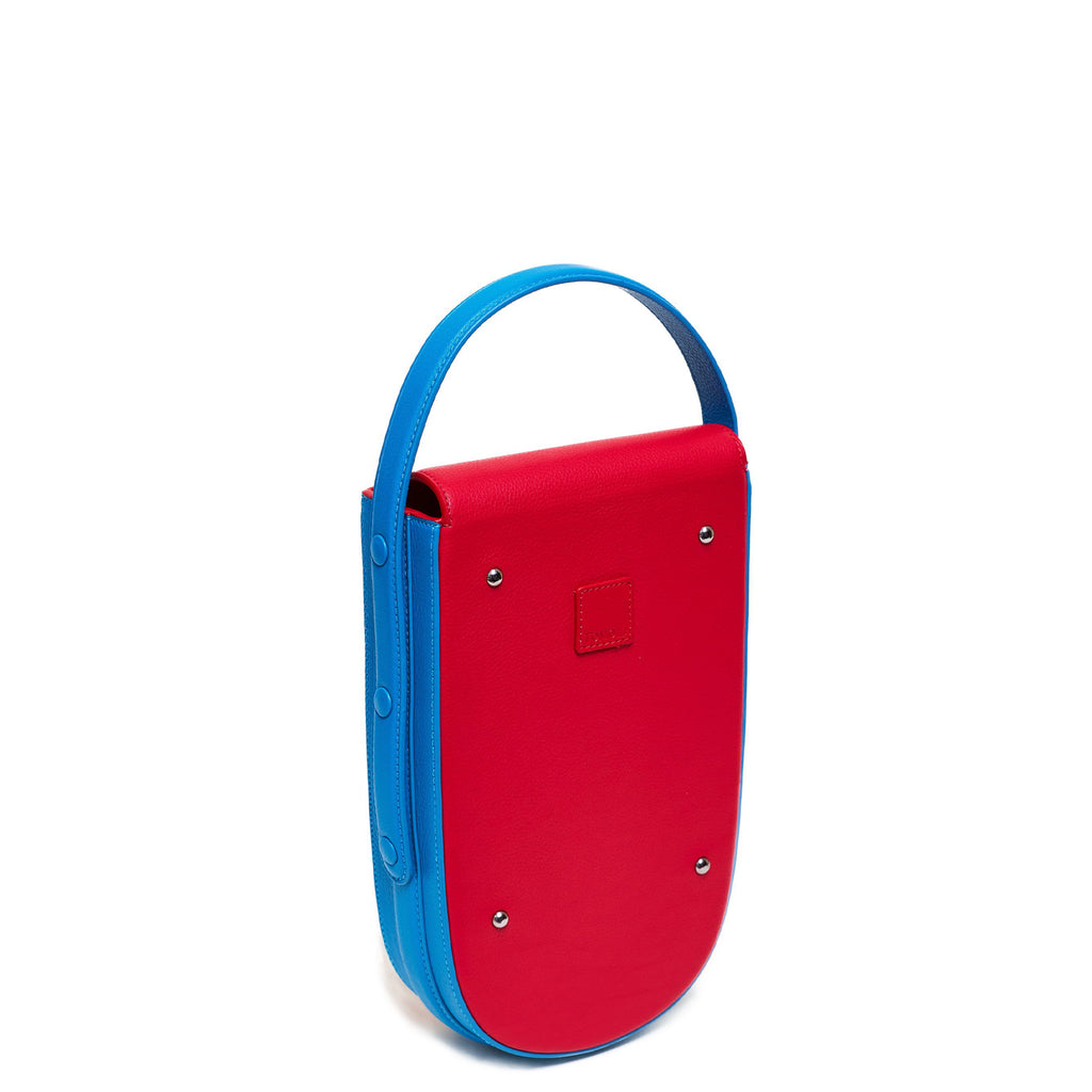 A colorful red and blue mini leather handbag. The handbag has an elongated rounded shape and a blue adjustable top handle. The hardware is gunmetal. This is the back view of the Tomoli Fitini bag in Sky Red.