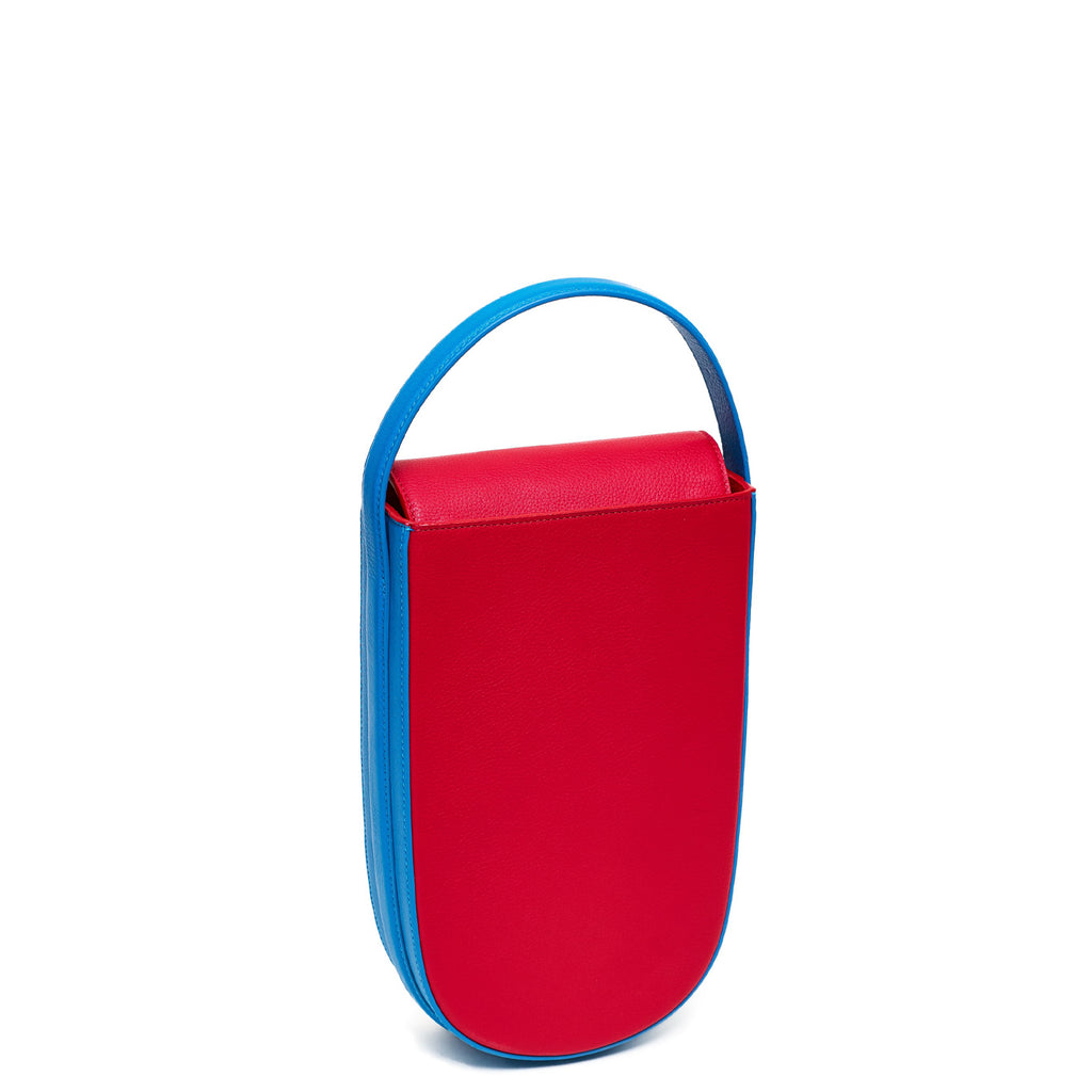 A colorful red and blue mini leather handbag. The handbag has an elongated rounded shape and a blue adjustable top handle. The hardware is gunmetal. This is the front view of the Tomoli Fitini bag in Sky Red.