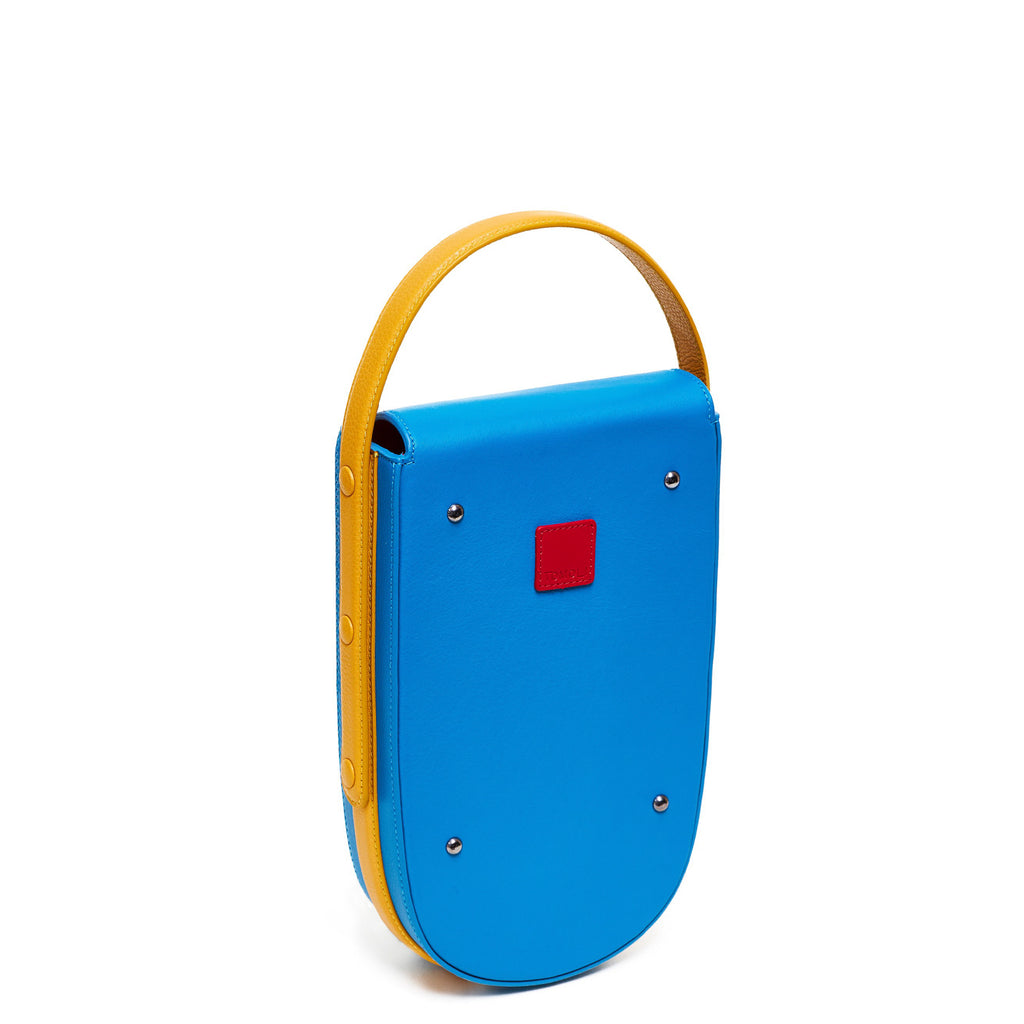 A colorful blue and yellow mini leather handbag. The handbag has an elongated rounded shape and an adjustable yellow top handle. The hardware is gunmetal. This is the back view of the Tomoli Fitini bag in Golden Sky.