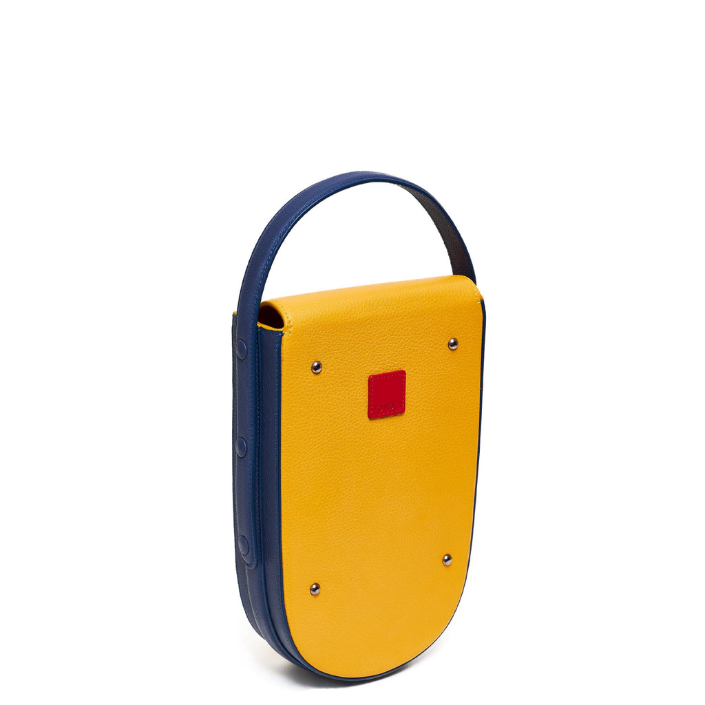 A colorful blue and yellow mini leather tote handbag. The handbag has an elongated rounded shape and a blue adjustable top handle. The hardware is gunmetal. This is the back view of the Tomoli Fitini bag in Shady Maize.