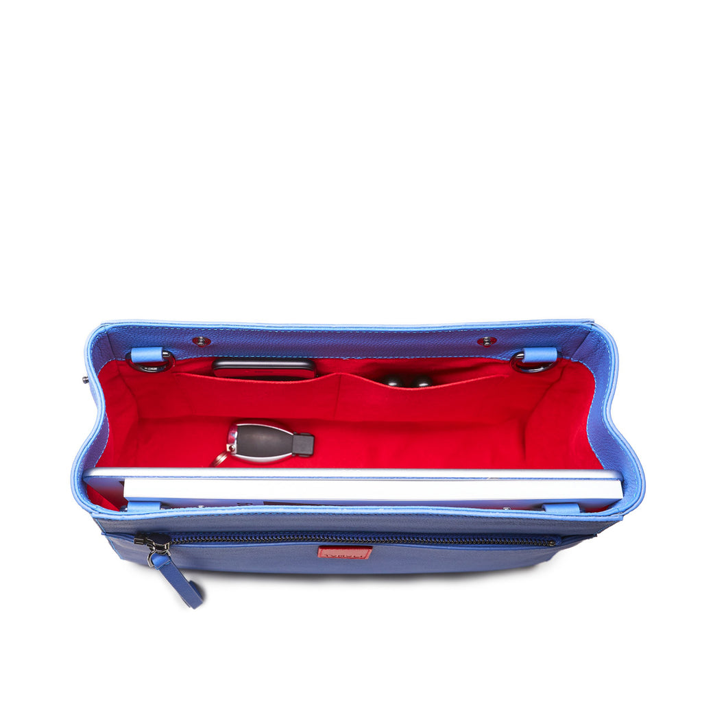 The product photo of a fashion handbag showing the interior of a blue purple leather bag. The bag has a bright red lining made of alcantara microsuede material. This is the interior view of the Tomoli Briffani Jut handbag in Hot Iris. This bag fits a laptop and a large iPad Pro tablet.
