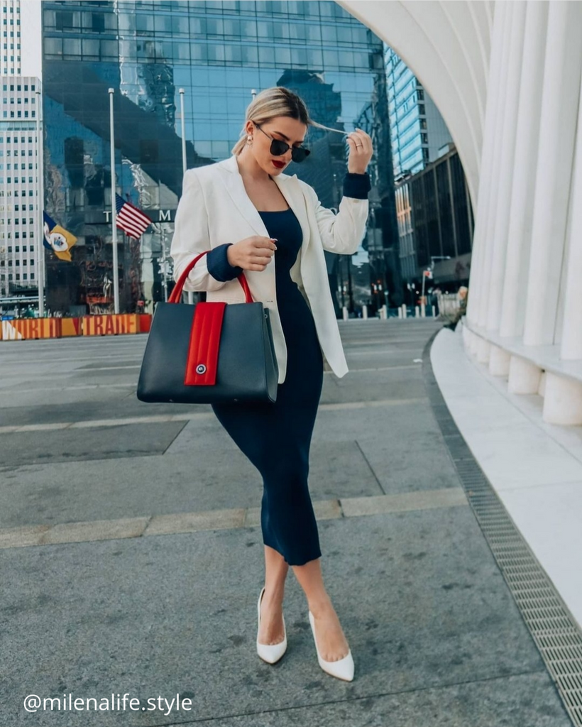A fashion and style inspiration photo showing influencer Milena Lifestyle wearing a black and white outfit and a color-blocked blue and red handbag.  The handbag has a classic trapeze shape with a straight quilted flap in the middle and top handles. This is the front view of the Tomoli Briffani Lean interchangeable tote handbag in Hot Denim. This bag can be used as an everyday bag, a work tote, or even an oversized clutch.