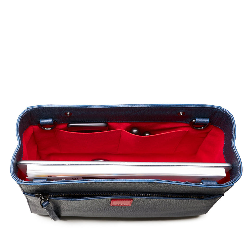 The product photo of a fashion handbag showing the interior of a dark blue leather bag. The bag has a bright red lining made of alcantara microsuede material. This is the interior view of the Tomoli Briffani Lean interchangeable tote handbag in Flirty Denim. This bag fits a laptop and a large iPad Pro tablet.