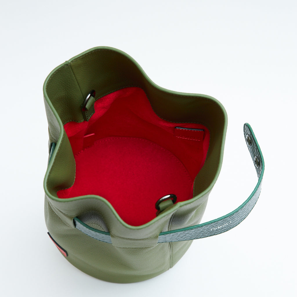 A product photo showing the interior of a leather bucket bag. The bag is olive green and has a red lining made of microsuede material. 
