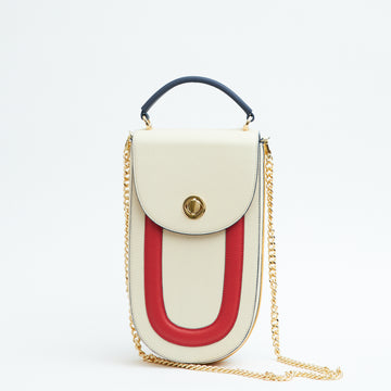 A fashion product photo showing the front view of a color-blocked off-white, blue and red leather handbag. The bag has an elongated rounded shape that resembles a saddle bag. The handbag has a flap closure with dark blue trims and a dark blue handle. There is a chain strap and a metal lock in gold hardware. This is the Tomoli Fitini II structured saddle handbag in Eclectic Ivory. This handbag can be used as an everyday crossbody bag, a work bag, or a special occasion bag.