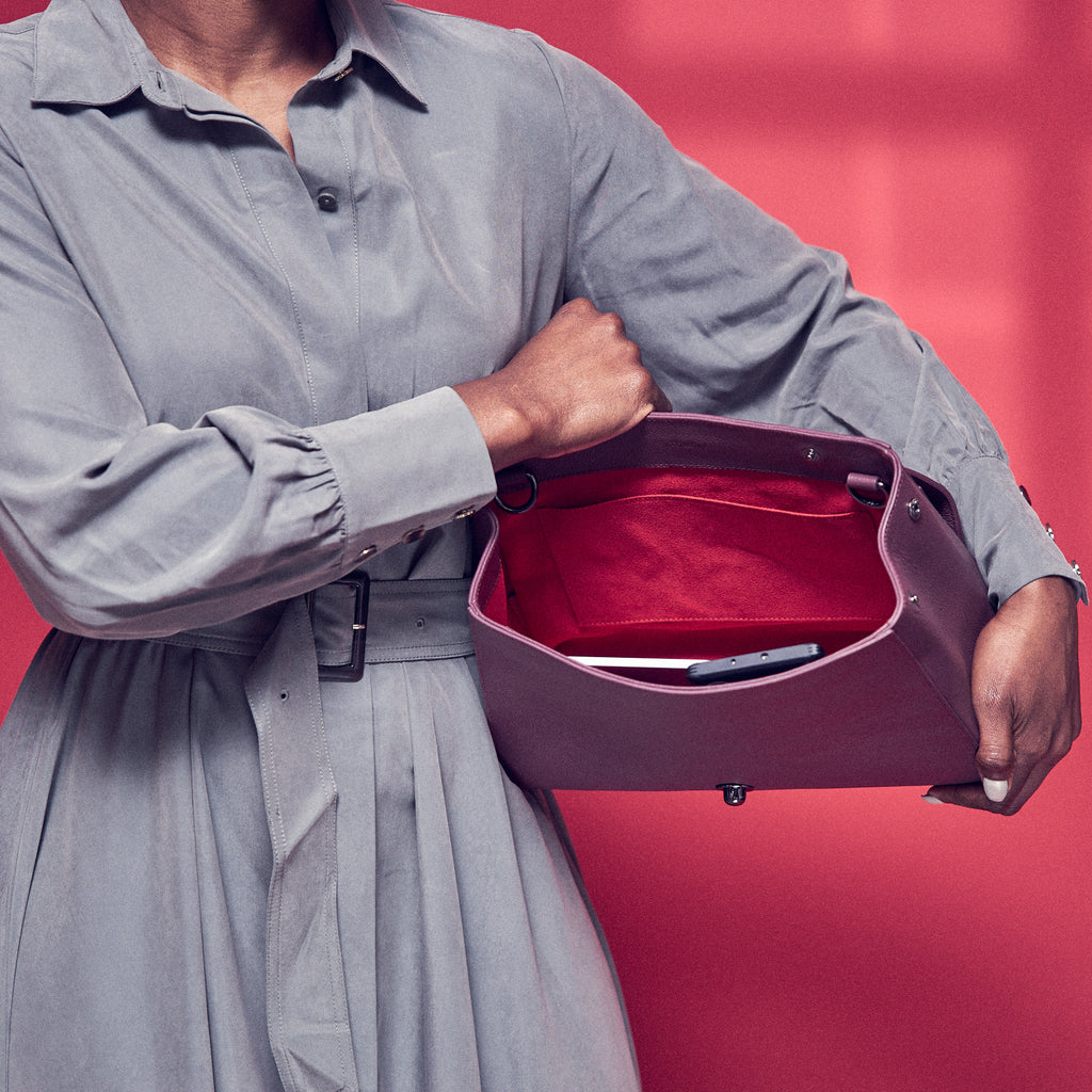The product photo of a fashion handbag showing the interior of a burgundy red leather bag. The bag has a bright red lining made of alcantara microsuede material. This is the interior view of the Tomoli Briffani Jut handbag in Sangria. This bag fits a laptop and a large iPad Pro tablet.