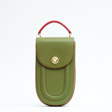 A fashion product photo showing the front view of a colorful green leather handbag. The bag has an elongated saddle shape with a flap closure, contrasting red trims, and a red top handle. There is a metal lock in gold hardware. This is the Tomoli Fitini II structured saddle handbag in Hot Olive. This handbag can be used as an everyday crossbody bag, a work bag, or a special occasion bag.